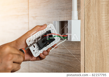 Hand of an electrician is using a screwdriver to attach the wires to the socket. Hand of an electrician is using a screwdriver to attach the wires to the socket. 82157795