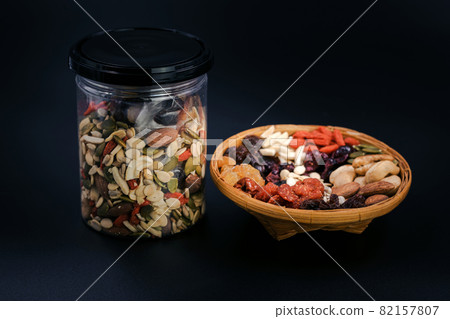 Whole grains and dried fruit in a bamboo plate and plastic bottle on black background. 82157807