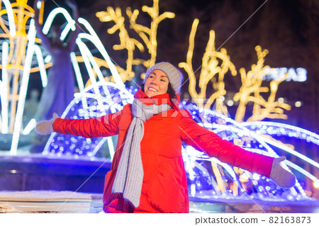 Winter holiday season. Christmas, New Year concept. Funny happy woman spend time having fun near illuminated and decorated showcase on city street. 82163873
