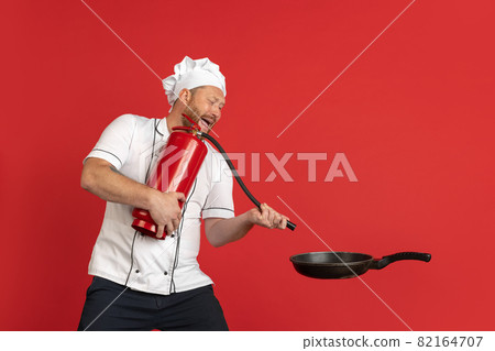 Comic portrait of hadsome bearded man, cook, male chef in white uniform having fun isolated on red studio background. Concept of job, occupation, humor. Comic portrait of hadsome bearded man, cook, male chef in white uniform having fun isolated on red studio background. Concept of job, occupation, humor. 82164707