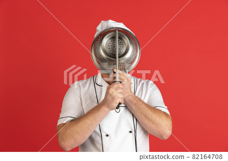 Comic portrait of hadsome bearded man, cook, male chef in white uniform having fun isolated on red studio background. Concept of job, occupation, humor. Comic portrait of hadsome bearded man, cook, male chef in white uniform having fun isolated on red studio background. Concept of job, occupation, humor. 82164708