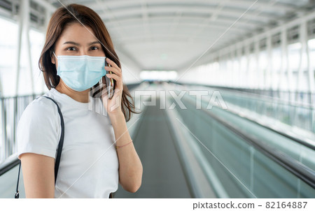 Portrait of a young woman in a medical mask for anti-coronavirus COVID-19 pandemic infectious disease outbreak protection and use a smartphone in Public area. Concept of Virus pandemic and pollution 82164887