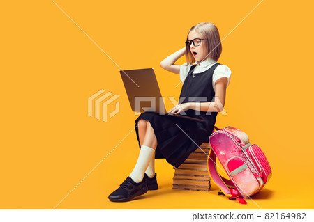 Full length shocked schoolgirl sit on the stack of books work on laptop. Kids education concept. 82164982