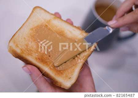 Woman spreading peanut butter on toast closeup Woman spreading peanut butter on toast closeup 82165487
