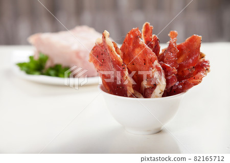 Jerky in a cup and raw meat with herbs on a white plate. Jerky in a cup and raw meat with herbs on a white plate. 82165712