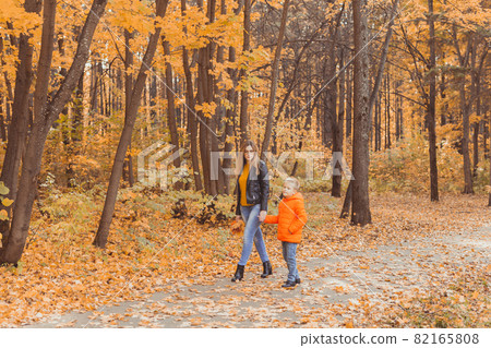 Mother and son walking in the fall park and enjoying the beautiful autumn nature. Season, single parent and children concept. Mother and son walking in the fall park and enjoying the beautiful autumn nature. Season, single parent and children concept. 82165808