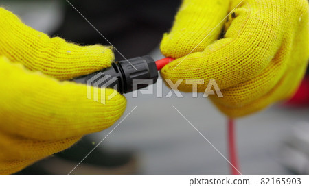 An electrician checks the wires. Special wire hardener at the power plant. An electrician in protective gloves installs wires. Connection of soy panels 82165903