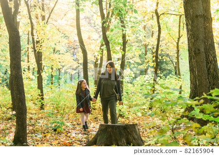 Asian mother and daughter walking holding hands at park. They are wearing warm clothes. Single parent lifestyle concept Asian mother and daughter walking holding hands at park. They are wearing warm clothes. Single parent lifestyle concept 82165904