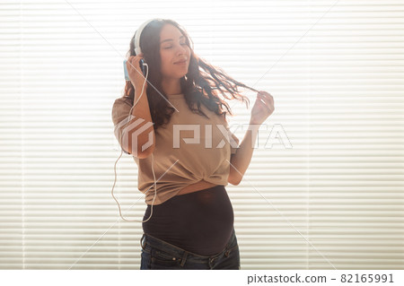 Pregnant woman listen to music in headphones at home and dances, copy space. Pregnant woman listen to music in headphones at home and dances, copy space. 82165991