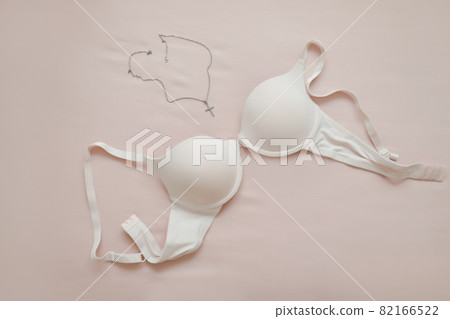 female white brassiere with jewelry on beige background female white brassiere with jewelry on beige background 82166522