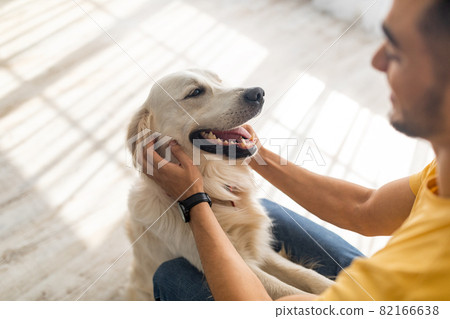 Best friend concept. Millennial Arab man scratching his dog on floor at home, selective focus Best friend concept. Millennial Arab man scratching his dog on floor at home, selective focus 82166638