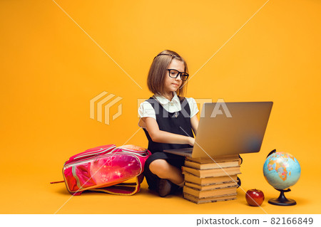 Full length caucasian schoolgirl sitting behind a stack of books working on laptop. Kids education Full length caucasian schoolgirl sitting behind a stack of books working on laptop. Kids education 82166849