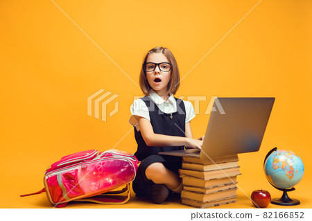 Full length surprised schoolgirl sitting behind a stack of books with laptop Kids education concept Full length surprised schoolgirl sitting behind a stack of books with laptop Kids education concept 82166852