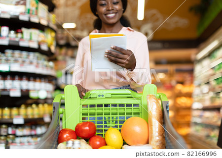 African American Lady Reading Grocery Shopping List Walking In Supermarket 82166996