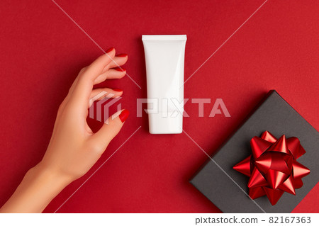Womans hand with tube of cream on red background. Self care beauty treatment concept. Womans hand with tube of cream on red background. Self care beauty treatment concept. 82167363