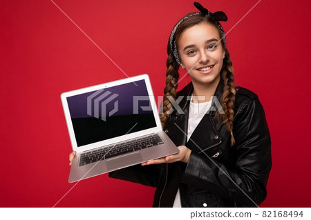 pretty happy smiling girl with brunette pigtails holding computer laptop wearing black jacket and 82168494