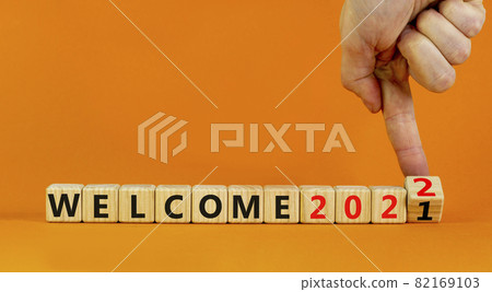Symbol of planning 2022 welcome new year. Businessman turns a wooden cube and changes words 'welcome 2021' to 'welcome 2022'. Beautiful orange background, copy space. Business, 2022 welcome concept. Symbol of planning 2022 welcome new year. Businessman turns a wooden cube and changes words 'welcome 2021' to 'welcome 2022'. Beautiful orange background, copy space. Business, 2022 welcome concept. 82169103