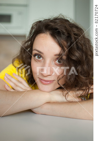 Beautiful curly girl in yellow t-shirt is looking at the camera at home in her apartment, posing with smile, happy people concept Beautiful curly girl in yellow t-shirt is looking at the camera at home in her apartment, posing with smile, happy people concept 82170724