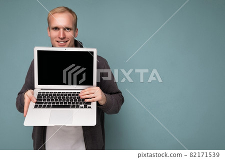 Close-up portrait of handsome smiling blonde man holding computer laptop with empty monitor screen Close-up portrait of handsome smiling blonde man holding computer laptop with empty monitor screen 82171539