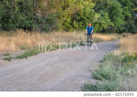 senior male cyclist is riding a touring bike on a gravel trail 82172054