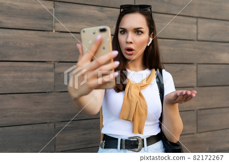 Photo of attractive shocked surprised young woman wearing casual clothes standing in the street 82172267