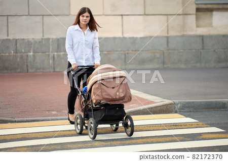 Young mother with child in baby carriage crosses crosswalk. 82172370