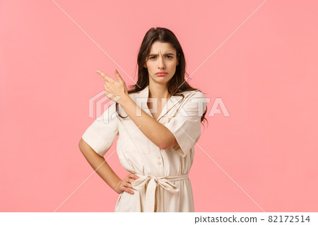 Something isnt right. Suspicious unsure young attractive brunette girl pointing upper left corner, frowning staring with disbelief, standing pink background unsure, asking question 82172514