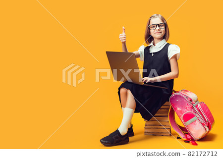 Full length smiling pupil sits on the stack of books with laptop shows thumb up. Kids education. Full length smiling pupil sits on the stack of books with laptop shows thumb up. Kids education. 82172712