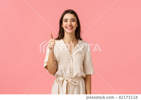 Giving positive feedback, recommendation. Good-looking cheerful, tender girl in gorgeous dress, showing thumb-up in approval, satisfied or advertising gesture, smiling like product, pink background 82173118