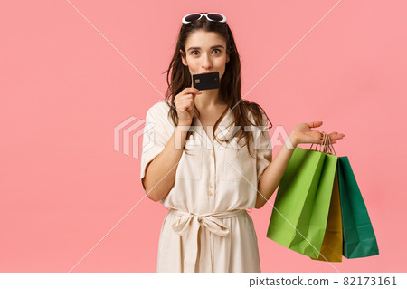 Girl likes wasting money on her credit card, kissing it and smiling joyfully, carrying shopping bags, shop in stores, getting new clothes, prepare gifts for girlfriends, standing pink background 82173161