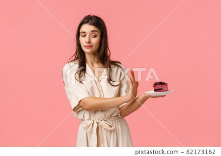No thank you. Girl having strong will, reject piece cake, holding plate and making stop, refusal motion with determined, assertive expression, standing pink background, stick to diet 82173162
