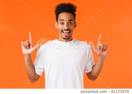 Excited and intrigued, enthusiastic african-american male in t-shirt, with moustache afro haircut, pointing fingers up, smiling amused, showing perfect product, shopping center, orange background Excited and intrigued, enthusiastic african-american male in t-shirt, with moustache afro haircut, pointing fingers up, smiling amused, showing perfect product, shopping center, orange background 82175879