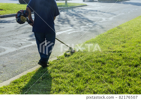A lawn mower mows fresh, green grass on the lawn near, a municipal worker with lawn mower in his hand. A lawn mower mows fresh, green grass on the lawn near, a municipal worker with lawn mower in his hand. 82176507
