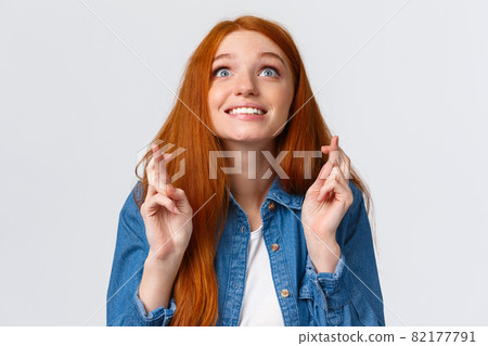 Excited and hopeful, optimistic cute redhead girl want dream come true, desire something, aspire achieve success good results, smiling looking up sky and making wish with fingers crossed good luck 82177791