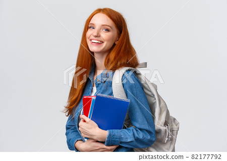 Teenagers, students and education concept. Cheerful lovely redhead female studying, going to univeristy or college, smiling carefree holding backpack and notebooks, standing white background 82177792