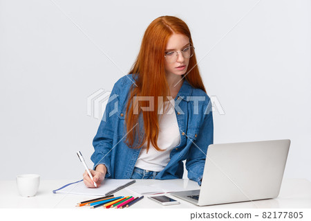 Inspiration, work and art concept. Focused busy cute redhead female in glasses, writing down notes from laptop, use useful website, online course to learn drawing, white background Inspiration, work and art concept. Focused busy cute redhead female in glasses, writing down notes from laptop, use useful website, online course to learn drawing, white background 82177805