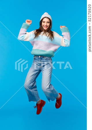 Vertical full-length portrait super happy girl jumping from amazement, celebrating new year, christmas party, enjoying holidays, shopping with awesome big discounts, smiling upbeat, blue background Vertical full-length portrait super happy girl jumping from amazement, celebrating new year, christmas party, enjoying holidays, shopping with awesome big discounts, smiling upbeat, blue background 82178920