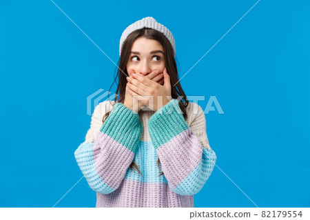 Oops, too loud. Cute and embarrassed silly young woman slipped tongue, said something unappropriate, close mouth with hands, looking sideways check nobody heard, standing blue background 82179554