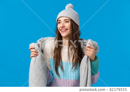 Attractive and carefree, dreamy pretty woman with long dark hair, wearing winter hat, sweater, wrapping scarf around neck going outside, ski and enjoying christmas holidays, look away smiling 82179555