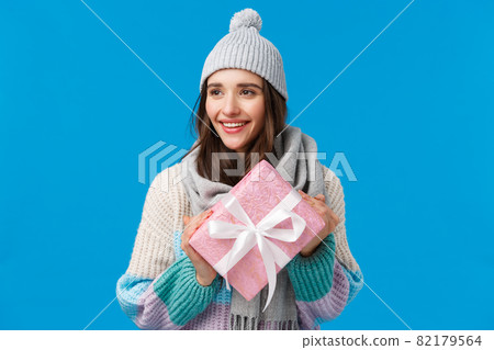 Holidays, christmas and valentines day concept. Romantic attractive young girlfriend 20s in scarf, winter hat and sweater, holding cute pink wrapped gift, prepared present for friend, smiling happy 82179564