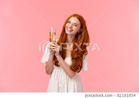 Carefree, excited cute redhead woman celebrating birthday, attend fancy party, wear white dress, laughing as discussing something with friends, raising glass champagne, drinking for success 82181054