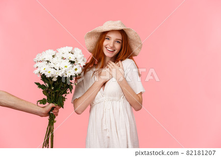 Touched, passionate and lovely alluring redhead female in straw hat, dress, touching heart and sighing with admiration and happiness, flattered for gift, hand extending her bouquet flowers Touched, passionate and lovely alluring redhead female in straw hat, dress, touching heart and sighing with admiration and happiness, flattered for gift, hand extending her bouquet flowers 82181207