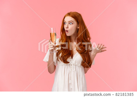 Wow this alcohol hits different. Amused and enthusiastic surprised redhead woman look amazed and wondered and glass with champagne, raising one hand and shrugging, stare curious 82181385