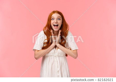 Fascinated, amused lucky redhead female in white dress, clap hands, applause from excitement and amazement, look camera astonished, feeling upbeat, winning prize, pink background 82182021