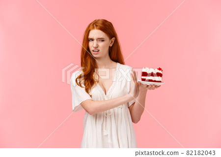 Take it away, gross. Ignorant and picky spoiled redhead birthday girl refusing eating dessert, holding plate with cake and making stop, rejection gesture, turn away with disgust, pink background Take it away, gross. Ignorant and picky spoiled redhead birthday girl refusing eating dessert, holding plate with cake and making stop, rejection gesture, turn away with disgust, pink background 82182043