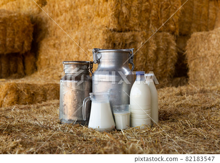 Fresh natural milk in decanter and cans on farm hayloft 82183547