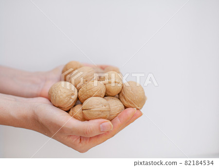 A lot of whole walnuts in women's hands on a white background close-up. Healthy, organic food with a high content of protein and protein. A lot of whole walnuts in women's hands on a white background close-up. Healthy, organic food with a high content of protein and protein. 82184534