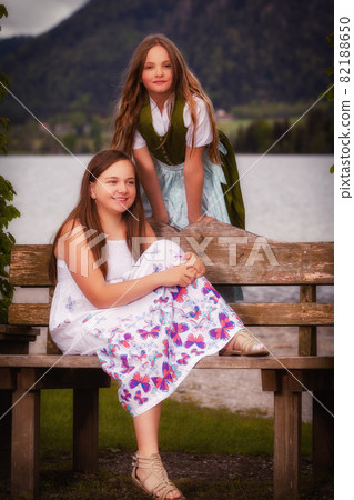 Two long haired young girls on a bench Two long haired young girls on a bench 82188650
