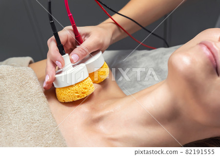 Close-up beautician doctor hand making anti-age face remodel procedure treatment with hardware microcurrent electric tool attractive young 30-40 female model at beauty clinic. Cosmetologist skincare Close-up beautician doctor hand making anti-age face remodel procedure treatment with hardware microcurrent electric tool attractive young 30-40 female model at beauty clinic. Cosmetologist skincare 82191555