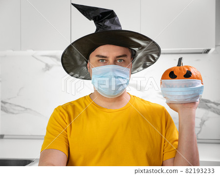 Man wearing medical mask and hold scary face pumpkin with protective mask. Celebration halloween at lockdown Man wearing medical mask and hold scary face pumpkin with protective mask. Celebration halloween at lockdown 82193233